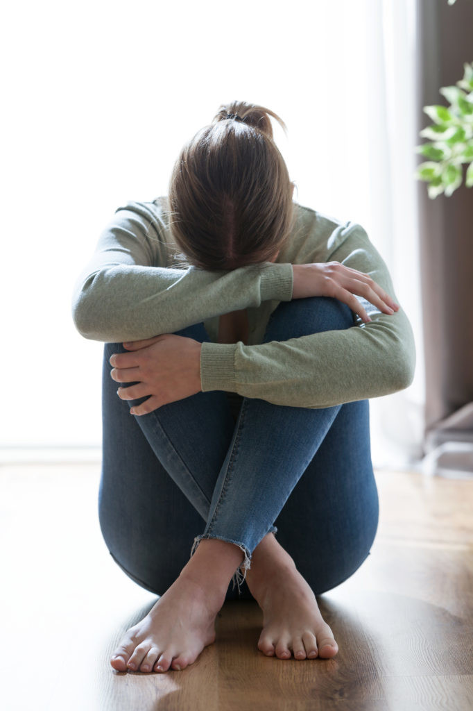 Unhappy lonely and depressed young woman hiding her face between legs at home.